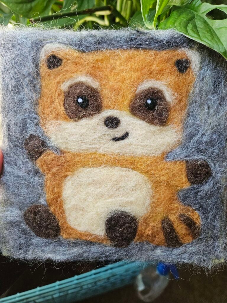 A smiling Spiffo rendered in wool, on a grey background.